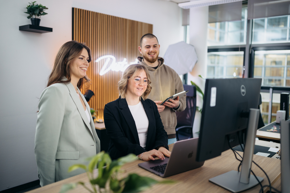 Drei Mitarbeitende stehen an einem Schreibtisch. Im Hintergrund leuchtet das Distart-Logo.